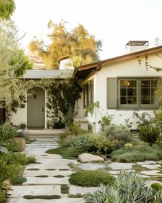 a white house with green shutters and stone path leading to the front door is surrounded by greenery