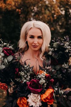 a woman with blonde hair holding a bouquet of flowers and greenery in front of her face