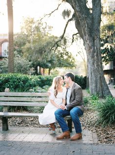 a man and woman sitting on a bench in front of a tree