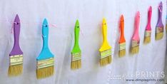 colorful paintbrushes are hung on a line with pink, yellow, and blue bristles