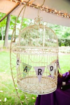 a white birdcage with the word card hanging from it's side on a purple table cloth