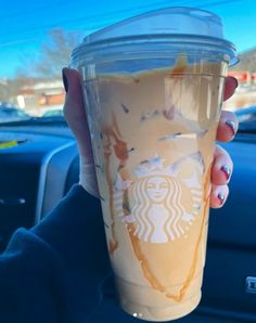 a woman holding up a starbucks cup in her hand while she's driving down the street