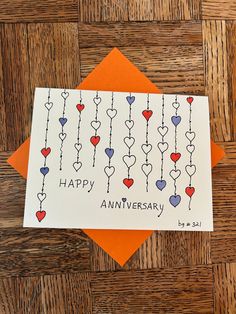 an anniversary card with hearts hanging from it on a wooden table next to orange envelope