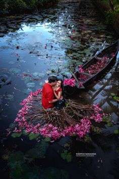 two people in a boat with pink flowers floating on the water and one person is kissing