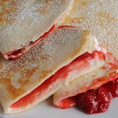 two crepes with strawberries are stacked on top of each other and covered in powdered sugar