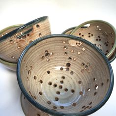 three ceramic bowls with holes in them on a white surface