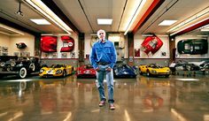 a man standing in the middle of a garage with several cars on display behind him