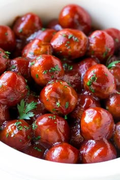 a close up view of some meatballs with sauce and parsley in a white bowl