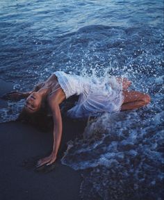 a woman is laying on the beach with her head in the water and arms out