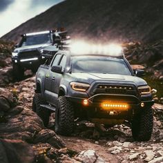 two trucks driving down a rocky road in the mountains