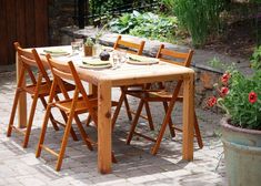 a wooden table with four chairs and plates on it in the middle of a garden