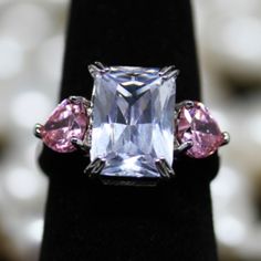 three stone ring with pink and white stones on it's sides, sitting on a black velvet stand