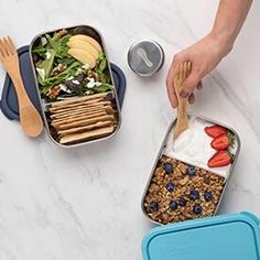 a person is holding two forks over some food in their lunch boxes on the table