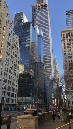 people are walking on the sidewalk in front of tall buildings with skyscrapers behind them