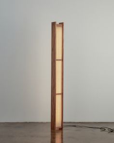 a wooden floor lamp sitting on top of a hard wood floor next to a white wall