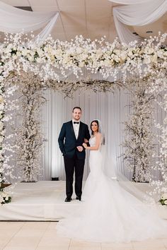 a bride and groom standing in front of an archway decorated with white flowers