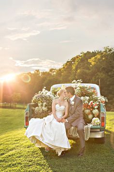 a bride and groom sitting in the back of a pickup truck with flowers on it