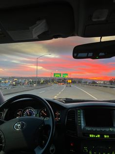 the view from inside a vehicle driving on a highway at sunset or dawn with traffic signs in the distance