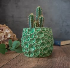 a small green cactus sitting on top of a wooden table next to a flower pot