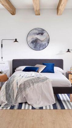 a bedroom with white walls and wood beams, a bed that has blue pillows on it