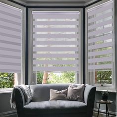 a couch sitting in front of two windows with white blinds on the top and bottom