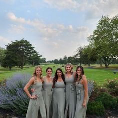 four bridesmaids pose for a photo in front of some lavender bushes and trees