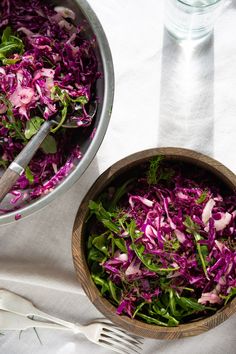 a wooden bowl filled with red cabbage and green onions next to a metal pan full of salad