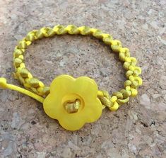 a yellow bracelet with a flower on it sitting on top of a stone floor next to a rock