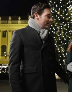 a man and woman standing in front of a christmas tree with lights on the building behind them