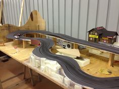 a model train set on a wooden table in a garage with toy cars and buildings