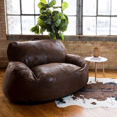 a brown leather chair sitting on top of a hard wood floor next to a potted plant