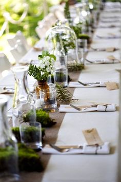 a long table is set with place settings and flowers in glass vases on it