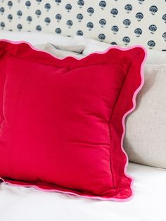 a red pillow sitting on top of a bed next to a white headboard and pillows