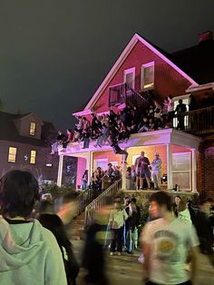 a group of people standing in front of a pink house at night with lights on