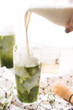 someone is pouring something into a glass with ice and cucumber slices in it