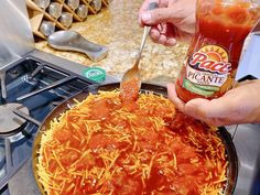 a person holding a spoon over a pizza in a pan with sauce and cheese on it