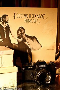 a camera and some books on a table with a poster behind it that says fleetwood mac rumours