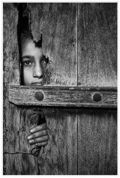 a girl peeking out from behind a wooden door with her hands on the handle and face