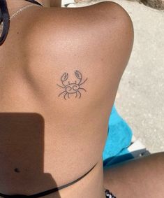 a woman's back with a small crab tattoo on her left side ribcage