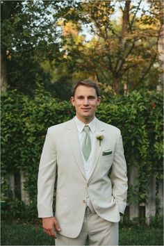 a man in a white suit and green tie posing for the camera with his hands in his pockets