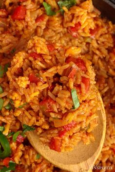 a wooden spoon filled with rice and tomatoes on top of a pan full of other food