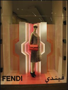 a mannequin dressed in a dress and purse stands behind a display case with the word fendi on it