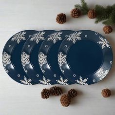 four blue plates with white snowflakes on them and pine cones next to them