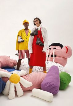 two women standing next to large stuffed animals on a white surface with one holding a handbag