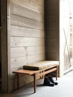 a wooden bench sitting in front of a wall next to a pair of black shoes