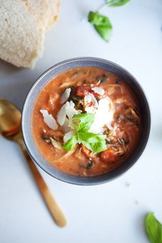 a blue bowl filled with soup next to a spoon and bread on a white table