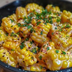 a bowl filled with corn covered in seasoning and sprinkled with parsley