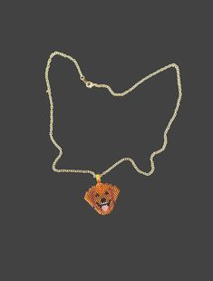 a necklace with an orange and yellow square pendant on a silver chain, hanging from a black background