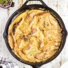 a skillet filled with chicken and cheese on top of a table next to some vegetables