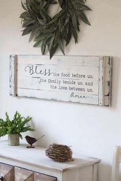 a wooden sign hanging on the wall next to a white dresser and potted plant